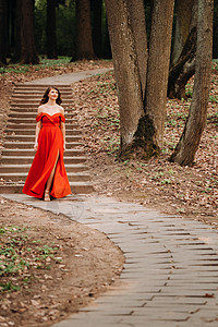 长着长发的长红裙子笑着女孩在树林中公园散步时身穿长红色礼服公主跑步奢华森林太阳童话魔法摄影海报派对成人高清图片素材
