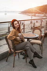 迷人的女人坐在春天的露天咖啡馆里享用她的咖啡 红色贝雷帽的法国妇女有都市背景的 晚上在城市街道上拿着咖啡杯的巴黎女人技术城市快乐背景图片