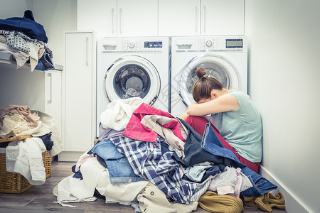 在洗衣房用蓝色音调的洗涤机 衣物放在洗衣间 感到不耐烦和紧张的女人蓝色的高清图片素材