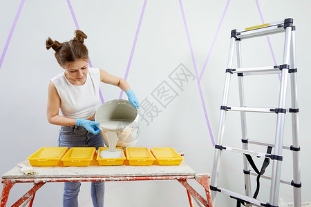 青年妇女将涂料倒入塑料油漆托盘公寓维修滚筒刷子女性装修梯子房子白色家居背景图片