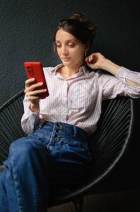肌肤暗沉美丽的卷发女孩在家里的公寓里 在暗底背景上 在快乐的人的概念下 使用红色智能手机背景