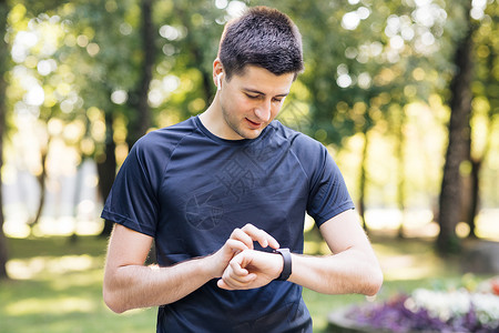 成年男子使用智能手表利用触摸屏 享受健康活跃的生活方式 男性跑者在夏令营从事心操锻炼活动;便携式现代耳机背景图片