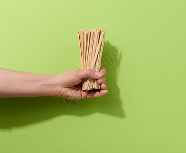 手持木棍的女人女性手持可支配木棍 用于在绿色背景下搅拌热饮 咖啡和茶匙背景