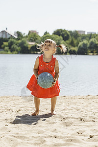 沙滩玩球的孩子穿红裙子的可爱小女孩 在沙滩上玩球赤脚喜悦玩具礼服活动家庭排球幸福竞赛海滩背景