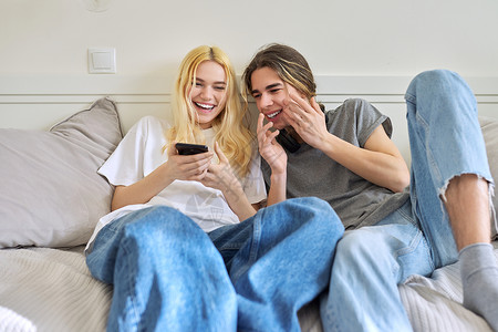 坐在沙发上 看着智能手机 玩得开心的青少年情趣相伴情绪幸福乐趣夫妻友谊女朋友潮人女士电话青年女性高清图片素材