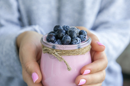 酸奶奶昔女手拿着碗 桌上放着酸奶和蓝莓 女人吃蓝莓酸奶和新鲜蓝莓 健康的早餐 超级食物健康吃素食素食背景