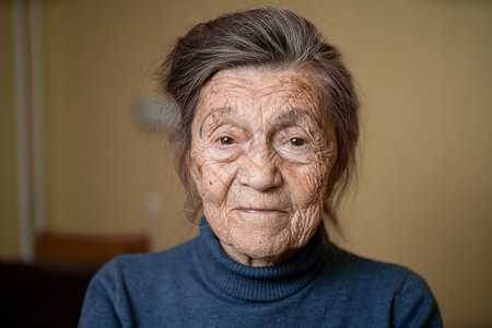 90 岁的可爱老妇人 头发花白 脸上有皱纹 穿着毛衣 肖像很大 微笑着 看起来很快乐 房间的背景 主题长肝抗衰 老人心情好疗养院背景图片