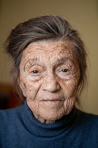 90 岁的可爱老妇人 头发花白 脸上有皱纹 穿着毛衣 肖像很大 微笑着 看起来很快乐 房间的背景 主题长肝抗衰 老人心情好悲伤成背景图片