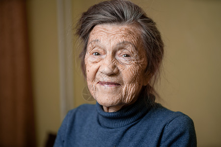 90 岁的可爱老妇人 头发花白 脸上有皱纹 穿着毛衣 肖像很大 微笑着 看起来很快乐 房间的背景 主题长肝抗衰 老人心情好老年悲背景图片