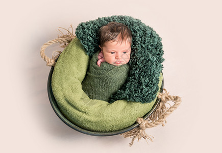 新生儿裹在绿色椰子里 躺在篮子里襁褓孩子休息帽子围巾工作室婴儿引擎眼睛女孩毛茸茸的高清图片素材
