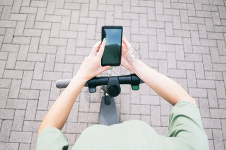 可移动板车女性在用电子摩托车站着时使用智能手机的视角背景