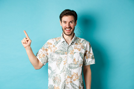 穿着Hawaiian衬衫的快乐青年左指 展示空洞的空间和微笑  旅游与度假  概念旅行广告工作室成人假期商业成功胡子男人男性背景图片