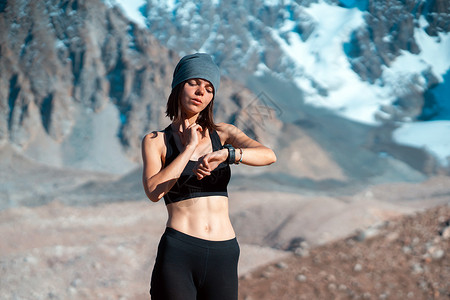 女孩看着她的手表 雪山在背景上运动蓝色有氧运动脉冲女性呼吸智能锻炼速度训练背景图片