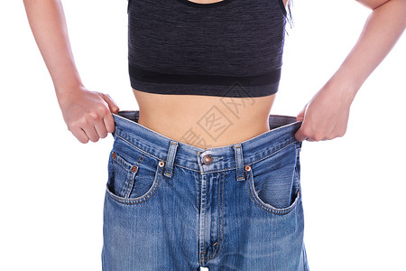牛仔裤女孩女人的特写展示了她的体重减轻 穿着白色背景中突显的旧牛仔裤减肥女孩腹部身体成人女性腰部裤子损失重量背景