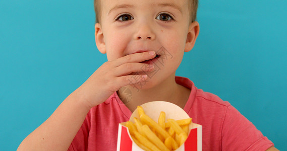 小男孩吃薯条室内小男孩在吃鱼和薯片时微笑蓝色油炸饮食男生背景童年马铃薯小吃筹码工作室背景