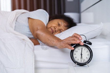 睡在床上的高级女人 按着清晨闹钟时的按声按钮退休成人苏醒睡眠压力女性就寝时间枕头休息沮丧高清图片素材