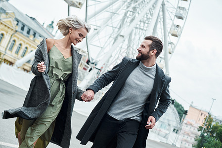 户外浪漫约会 在娱乐公园奔跑的年轻夫妇手牵着手 面带微笑 开心地看着对方背景图片