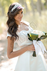 美丽的新娘在森林中户外的美丽新娘花束白色绿色女性发型女孩婚礼裙子女士年轻的高清图片素材