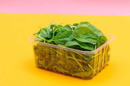 黄色背景透明塑料套件中新鲜的婴儿菠菜叶新片减肥饮食蔬菜排毒树叶食物植物活食生食沙拉背景图片