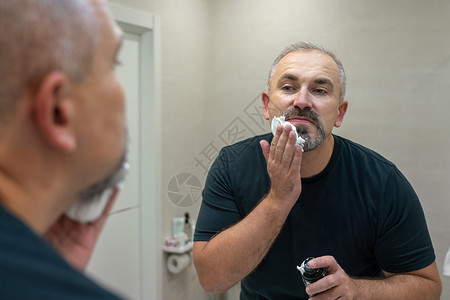 长得英俊的灰发白头发中年男子的肖像 他们用剃须泡沫来修剪胡子早晨高清图片素材