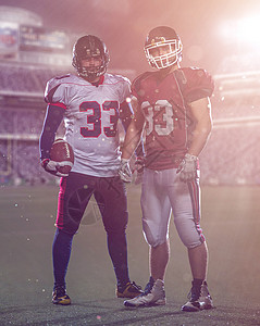 球员站立拍球两名美国足球运动员站在球场上站立竞争体育场头盔运动装球员场地男性竞赛团队力量背景