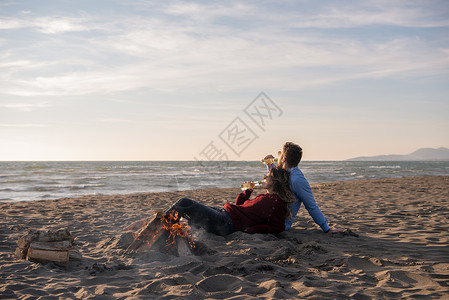 火车上的日落春火旁的海滩上坐着年轻夫妇 喝啤酒女孩篝火男人闲暇喜悦友谊海洋朋友们啤酒假期背景