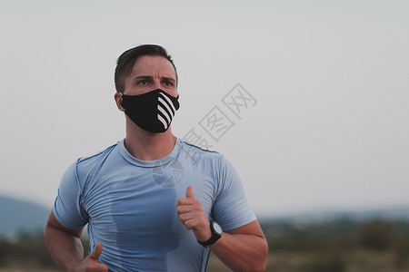 戴口罩跑步冠状病毒爆发期间 身穿湿运动服 戴着黑色防护面罩的健身男子在城市户外跑步 Covid 19 和体育慢跑活动运动和健身 新常态训练背景