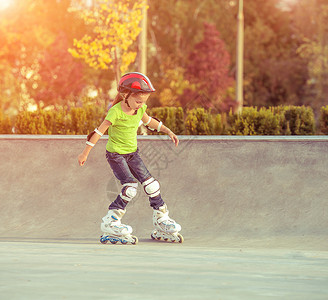 滑冰的小女孩穿溜冰鞋的小女孩头盔婴儿乐趣闲暇女孩学校安全公园享受孩子背景