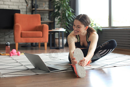 健身美丽苗条的女人在家里的客厅里做健身伸展运动 留在家里活动 运动 健康的生活方式成人互联网女士训练重量运动装体操身体肌肉瑜伽房子高清图片素材