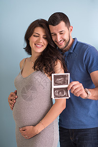 怀孕照片寻找蓝色背景上孤立的超声波照片的一对夫妇婴儿微笑夫妻母亲父亲丈夫腹部怀孕成人妻子背景