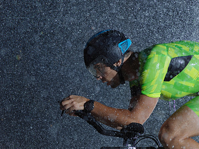下雨之夜骑自行车的三重运动员速度耐力训练钢铁侠活力赛车手头盔男人铁人竞赛背景