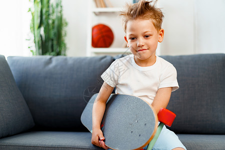 小男孩坐在沙发上坐在家里 拿着滑板背景图片