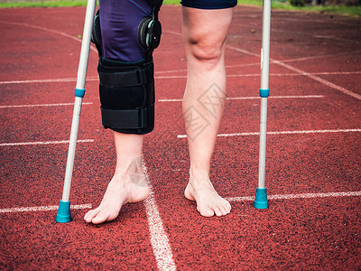 脚戴铁球骑拐杖的女运动员 戴着手腕支架和膝盖支撑疼痛多样性体育场运动伤害肌肉扭伤赤脚损伤韧带背景