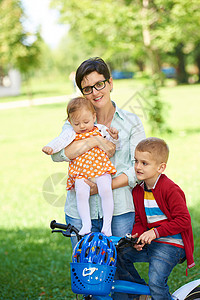 公园中快乐的年轻家庭喜悦孩子妈妈儿子闲暇女士自行车婴儿童年女儿关心高清图片素材