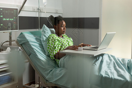非裔美国病人躺在床上看笔记本电脑上网上喜剧电影背景图片