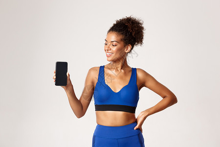体育和技术概念 健康的非洲裔美国女运动员 看起来很高兴 展示智能手机屏幕 白色背景背景图片