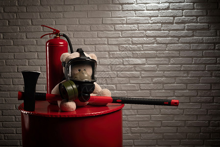 消防队的吉祥物是一只戴防毒面具 配有灭火器和烟雾红斧的泰迪熊背景图片