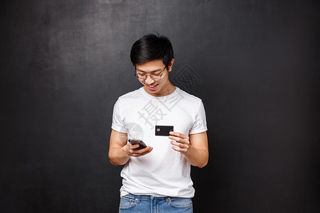 焕新衣银行 金融和支付概念 身穿 T 恤的亚洲年轻人 在购物应用程序中持有信用卡作为插入账单信息 微笑着看着手机显示屏 在网上购买新衣背景