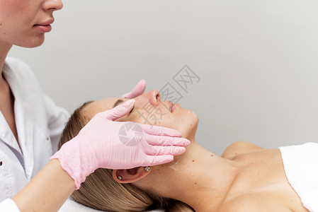 放松的年轻女子睡在沙发上 而美容师则按摩她的脸部并净化她的皮肤 Spa治疗程序化妆师女孩医生沙龙化妆品奶油女性面具护理手高清图片素材