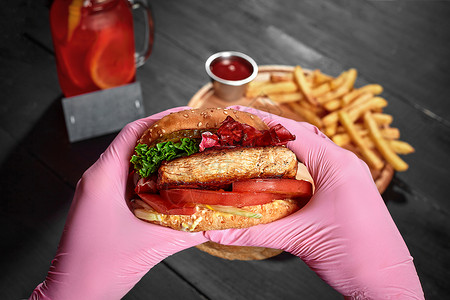 手托盘子手握粉红橡胶手套 包着汉堡 配有猪肉牛排 泡菜 新鲜蔬菜背景