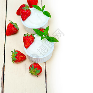 一粒刨开的草莓希腊有机酸奶和草莓薄荷早餐旋转叶子饮食小吃乳制品木头牛奶水果背景