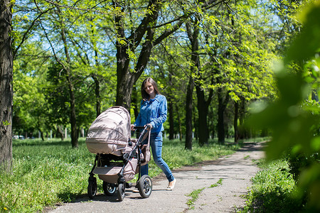 母亲推着婴儿车年轻母亲在公园里走路 推着婴儿车家庭越野车人行道女儿女孩父母孩子成人女性妈妈背景