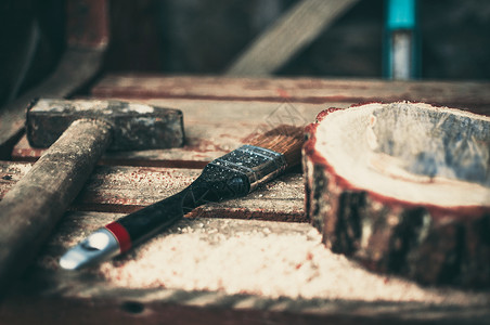 长凳上放着一把生锈的旧锤子 一把油漆刷和一根带木屑的圆形松木梁 大师班食物的木架 自己动手做的概念手锯手工具木工水平劳动松树工业背景图片