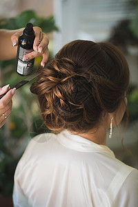婚礼沙龙主设计师用喷漆修补使新娘婚纱的发型化妆品女士梳子沙龙治疗美发理发师白花裙子女性背景