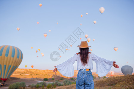 热气球和女孩在土耳其卡帕多西亚观看热气球的日出快乐妇女岩石蓝色飞机吸引力工作悬崖女士胡同女孩日落背景