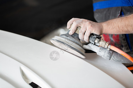 一名男子 他用研磨机刮沙 在汽车服务中为汽车制成油漆;修理工修车漆背景图片