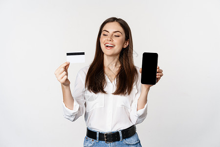 快乐的女人展示信用卡和智能手机屏幕 网上购物的概念 在应用程序中购买 站在白色背景上微笑顾问女性商务网络管理人员商业女孩工人工作店铺高清图片素材