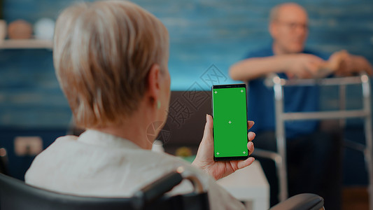 坐在轮椅上的高级妇女拿着绿色屏幕的智能手机高清图片