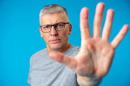 中年年年高龄蓝背景男子用手掌做停牌标记苦的高清图片素材