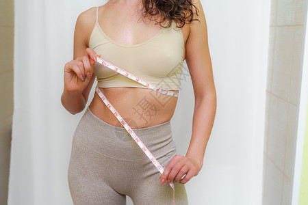 在家里用卷尺测量腰围的苗条女人的剪影 特写 一位面目全非的欧洲女性在室内检查减肥饮食或抽脂的结果 健康的生活方式动机训练身体磁带背景图片